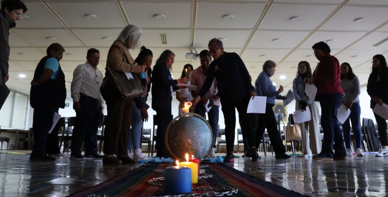 Un grupo de laicos y laicas rodea un globo terráqueo con velas encendidas durante una celebración
