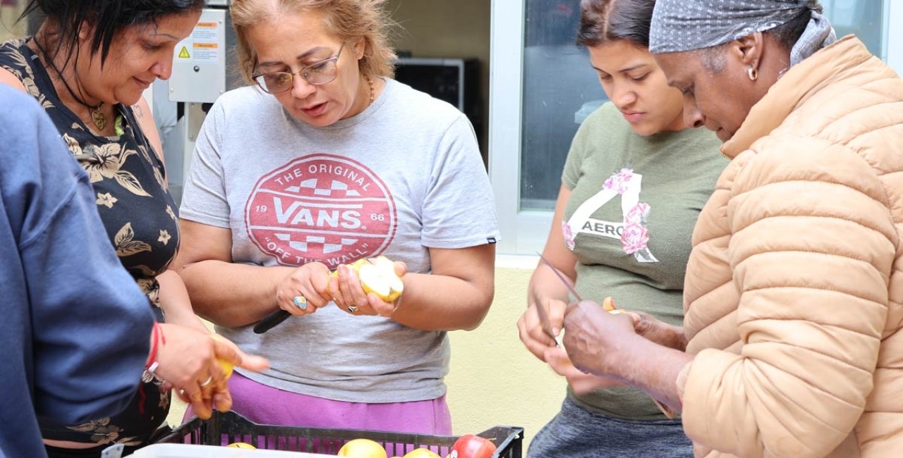 Cuatro mujeres pelan manzanas alrededor de una mesa, en una actividad comunitaria al aire libre
