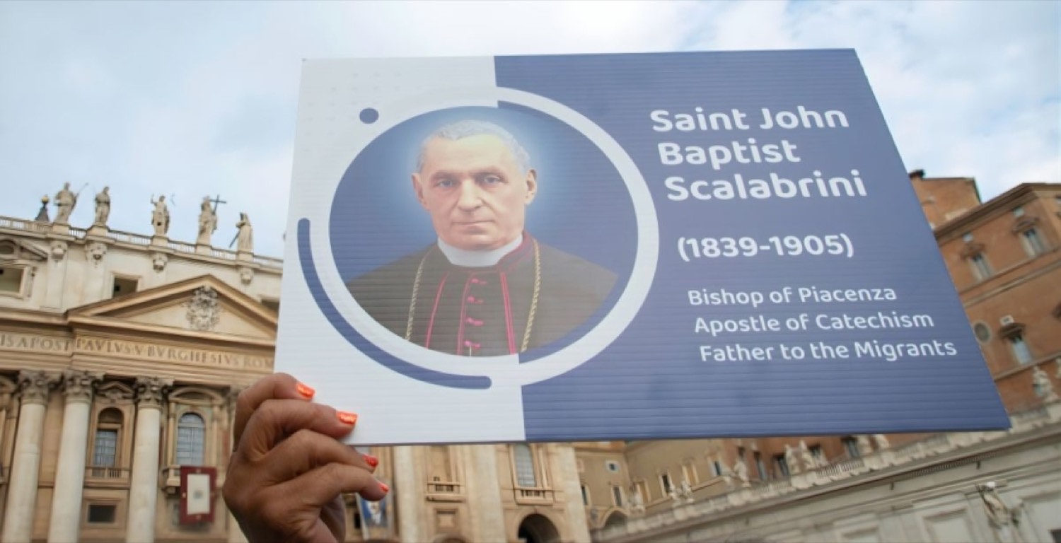 Una mano sostiene un cartel con el retrato de San Juan Bautista Scalabrini frente a la basílica de San Pedro
